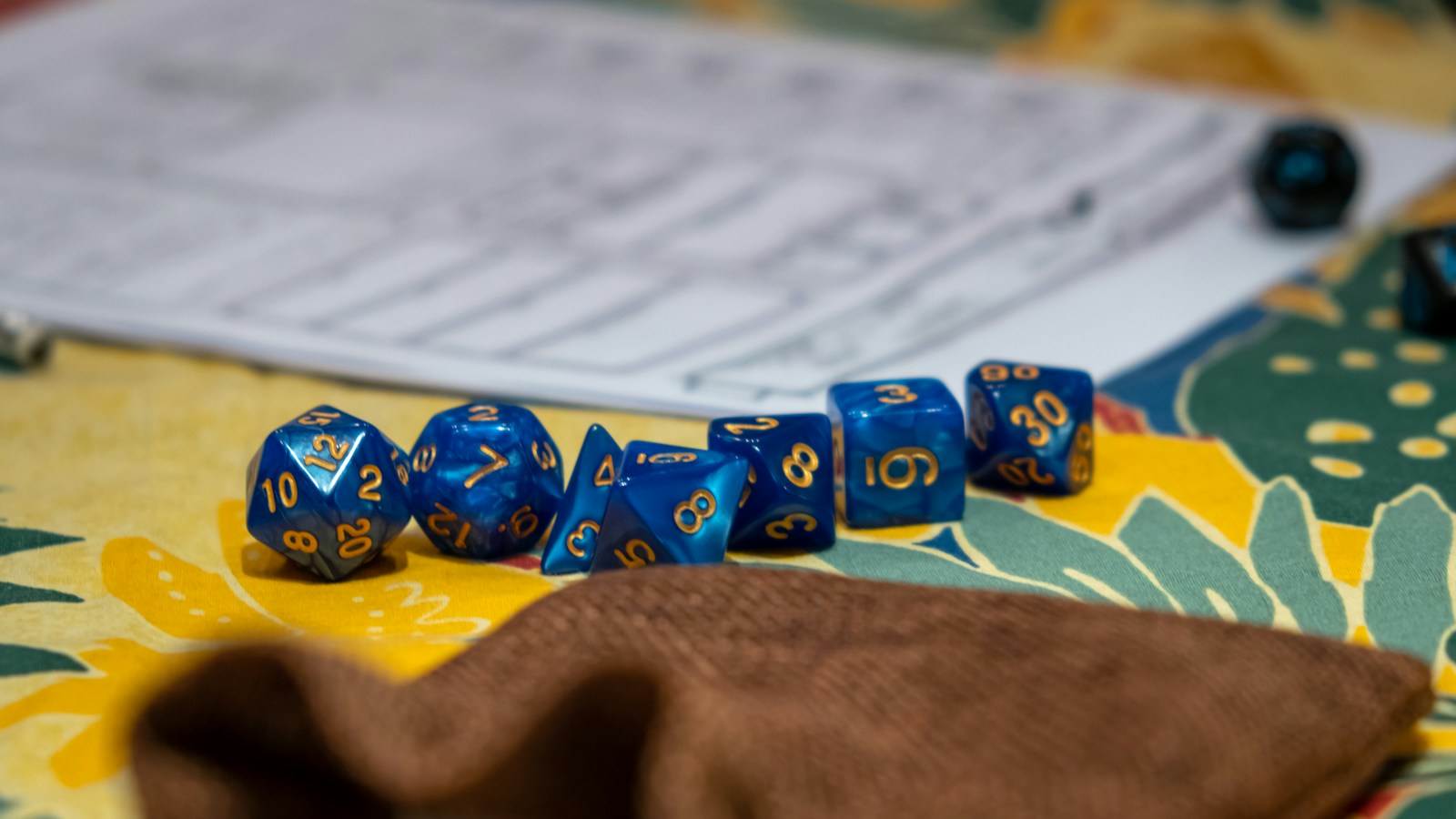 Blue role-playing dice beside a character sheet and a brown dice pouch.